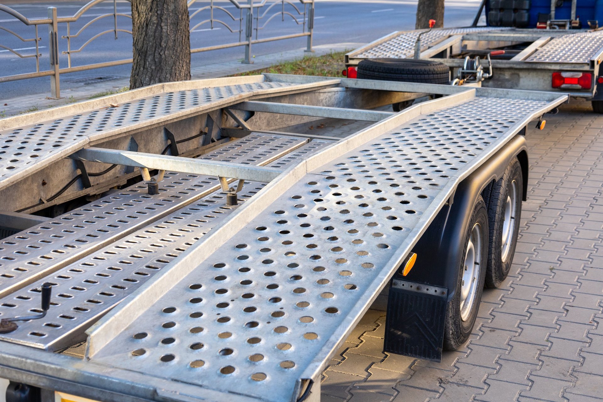 Large transport trailer with perforated surface and ramps parked in a city environment, showcasing its sturdy design under clear sky.