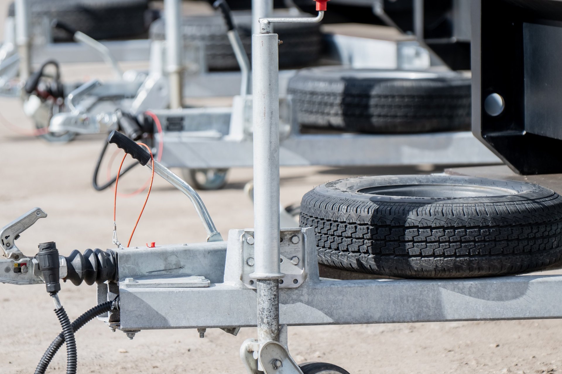 Galvanized steel trailer frames with hitch couplings and spare tires organized in a row for commercial transport and cargo logistics at an equipment rental dealership