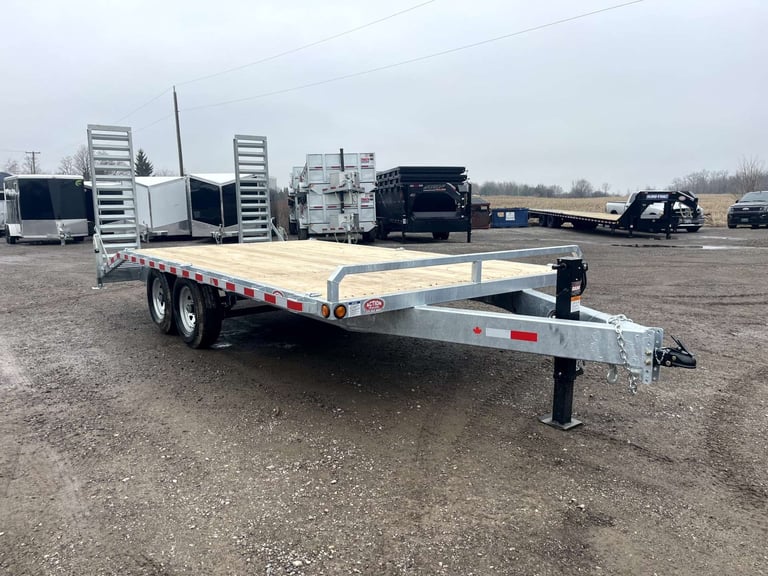 Tandem axle flatbed utility trailer with wooden deck parked in lot with other trailers in background