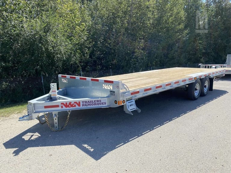 NAG enclosed flatbed trailer with wooden deck parked on asphalt, trees visible in background