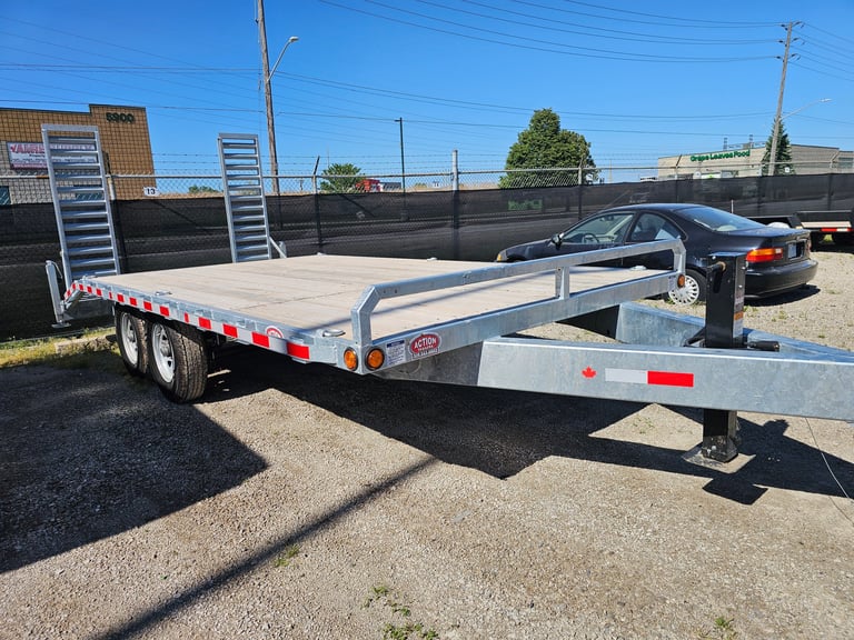 Empty aluminum utility trailer parked in a lot with industrial buildings and clear blue sky in background