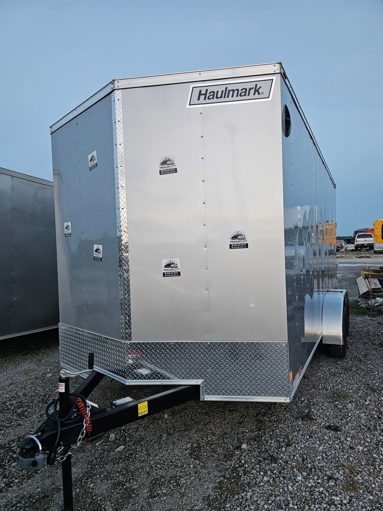 White Haulmark enclosed cargo trailer with black coupler and diamond plate trim on gravel lot