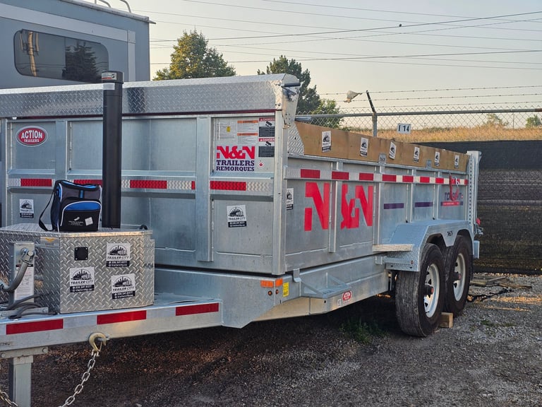 Silver and red utility trailer with storage compartments parked in a lot near a brick building